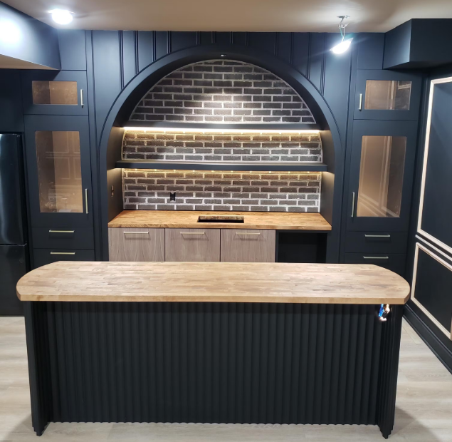 Modern kitchen with black cabinets, wooden island, and brick backsplash.